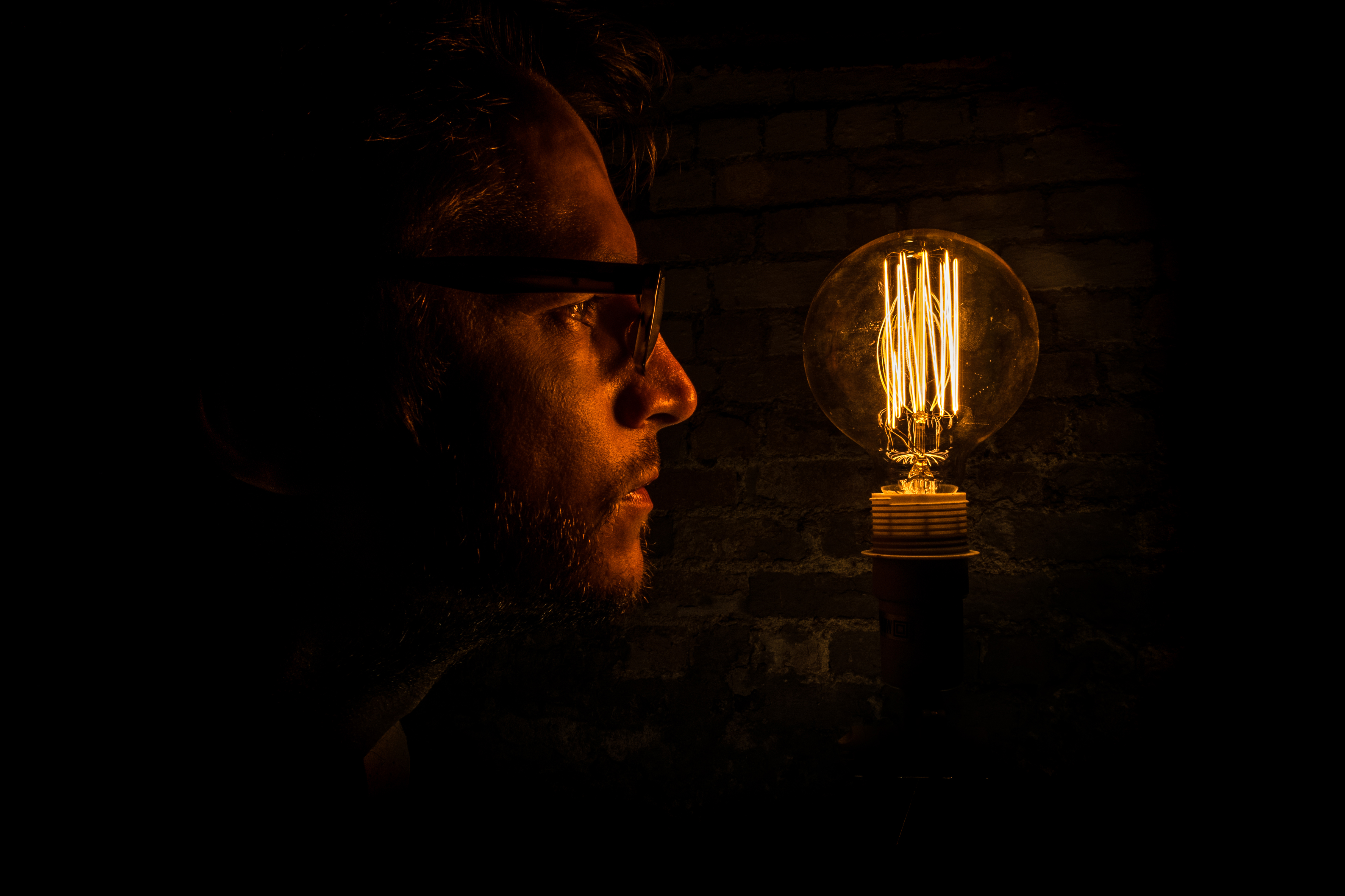 Dark photo of a man staring at a light bulb.