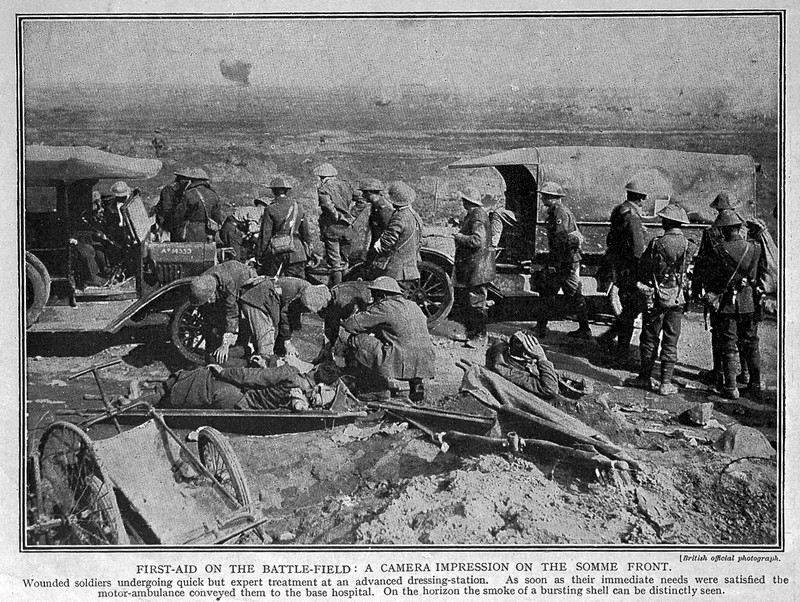 FIRST-AID ON THE BATTLE-FIELD: A CAMERA IMPRESSION ON THE SOMME FRONT. Wounded soldiers undergoing quick but expert treatment at an advanced dressing-station. As soon as their immediate needs were satisfied, the motor-ambulance conveyed them to the base hospital. One ht horizon the smoke of a bursting shell can be distinctly seen. 