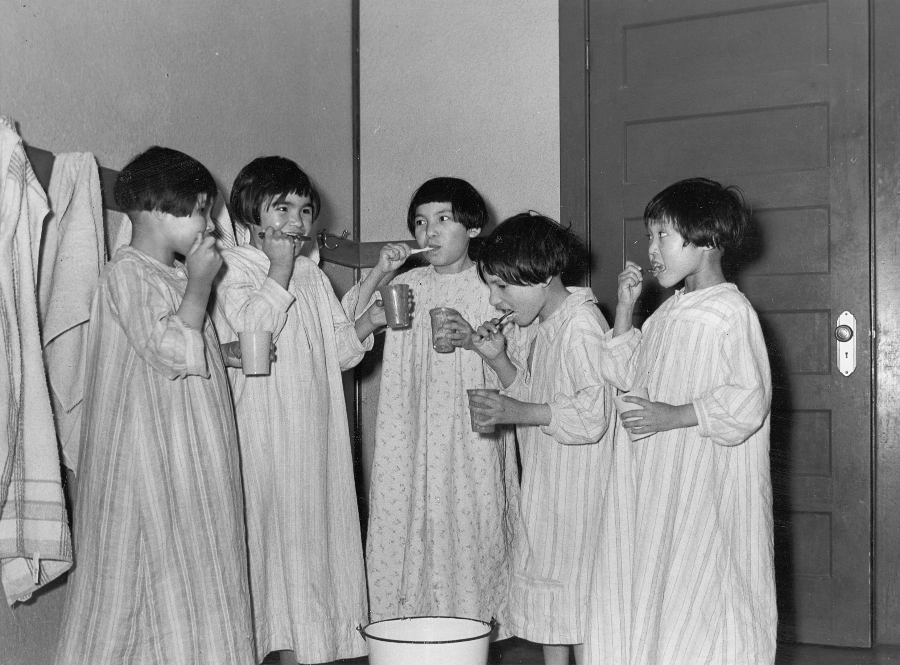 Black and white photo of girls brushing their teeth.